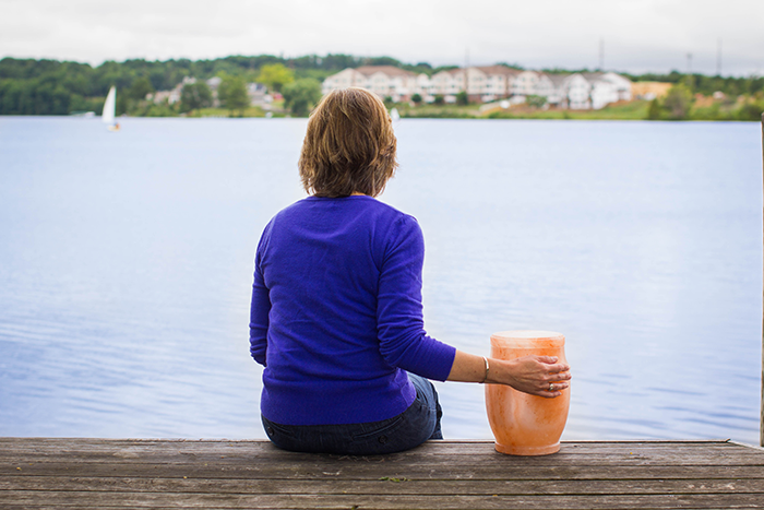 Woman sitting by the water with a cremation urn beside her, reflecting after the cremation process.